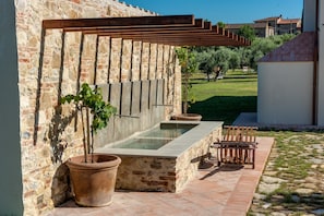 Un muro de piedra con una pérgola de madera, una fuente rectangular y un banco.