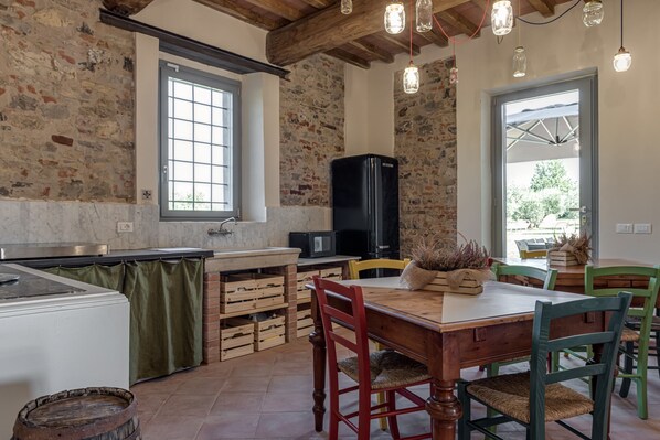 Una cocina rústica con una mesa de madera, sillas y un refrigerador.