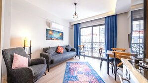 Een moderne woonkamer met een bank, fauteuils, een eettafel en een groot raam met blauwe gordijnen.