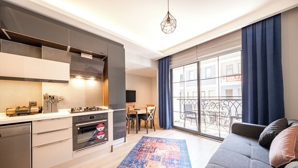 Een moderne keuken met inbouwapparatuur, een eethoek met een tafel en stoelen, en een groot raam met gordijnen.