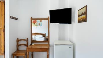 A bedroom with a wooden bed, a small table, a mirror, a television, and a refrigerator.