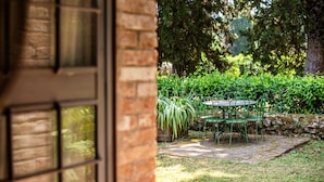 Un patio con una mesa y sillas, rodeado de follaje y un muro de piedra.