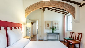 Un dormitorio con una cama grande, un arco de ladrillo, un escritorio con lámpara y una ventana con cortinas.