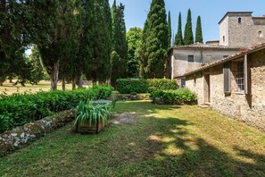 A courtyard with a stone building, a grassy area, and tall trees.