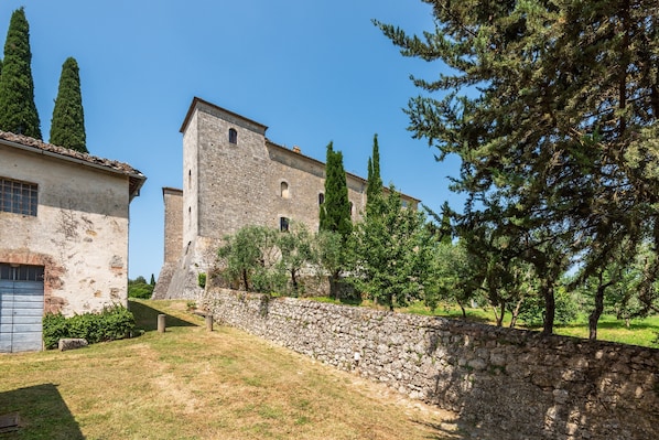 A stone building with a tower, surrounded by trees and a stone wall.