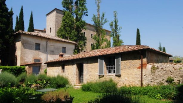 Un edificio de piedra con techo de tejas, rodeado de vegetación y árboles.