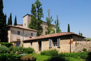 A stone building with a tiled roof, surrounded by greenery and trees.