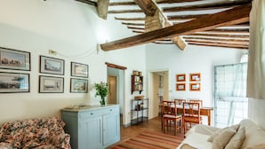 Una sala de estar con un sofá floral, un mueble azul claro, una zona de comedor con una mesa y sillas de madera, y una cocina visible al fondo.