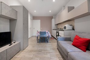 A modern living room with a grey sofa, a red pillow, a TV, and a dining area with a table and chairs.