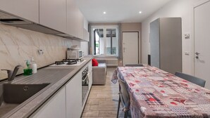 Une cuisine moderne équipée d’une cuisinière intégrée, d’un évier et d’un four à micro-ondes. On y trouve également un coin repas avec une table et des chaises, et une vue sur un balcon accessible par une porte vitrée.