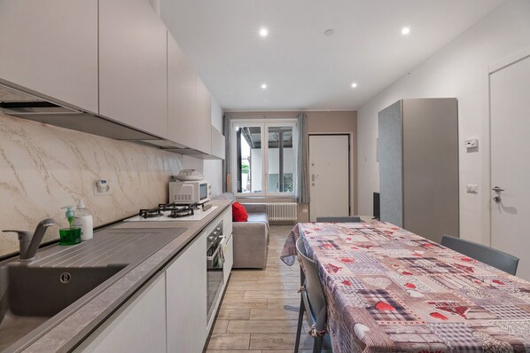 A modern kitchen with a built-in stove, a sink, and a microwave. There is a dining area with a table and chairs, and a view of a balcony through a glass door.