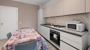 Une cuisine compacte équipée d’un four à micro-ondes, d’une cuisinière et d’un four, d’une table à manger recouverte d’une nappe à motifs et d’une porte.