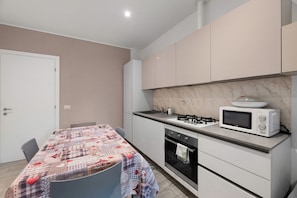 A compact kitchen with a microwave, stove, and oven, a dining table with a patterned tablecloth, and a door.