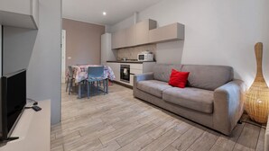 Un salon moderne comprenant un canapé, un téléviseur, une table à manger avec des chaises et un coin cuisine équipé d’un four à micro-ondes.