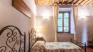 Ein Schlafzimmer mit einem Bett, einem Nachttisch, einem Fenster mit Vorhängen und einer Wandleuchte.