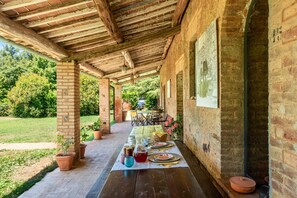 Une terrasse extérieure avec une table en bois dressée pour le repas, entourée de murs en briques et de plantes en pot.