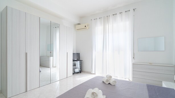 Ein modernes Schlafzimmer mit Bett, Kleiderschrank, Spiegel und Fernseher.