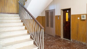 Eine Treppe mit Metallgeländer, Holzwandverkleidung, Marmorboden und einer Tür mit Lichtschalter.