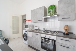 Een moderne keuken met een wasmachine, magnetron, fornuis, oven en een plant op het aanrecht.