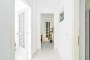 Een gang met witte muren, een kamerplant en een deur naar een andere kamer.