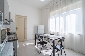 Eine Küche mit Herd, Mikrowelle und Kühlschrank, einem Esstisch mit Stühlen, einer Tür und einem Fenster mit durchsichtigen Vorhängen.