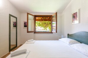 Ein Schlafzimmer mit Bett, Fenster mit Aussicht, Spiegel und einem Wandbild.
