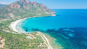 Vue aérienne d’une zone côtière avec une montagne, une plage et des eaux d’un bleu limpide.