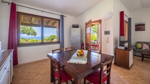 Un coin repas avec une table dressée pour quatre personnes, une vue sur la mer par la fenêtre et une petite cuisine en arrière-plan.