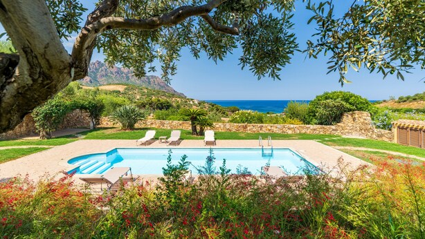 Une piscine avec des chaises longues, un mur en pierre et une vue sur la mer.
