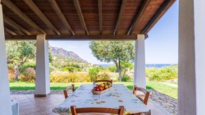Une terrasse couverte avec une table dressée pour le repas, entourée de chaises, et offrant une vue sur un paysage montagneux.
