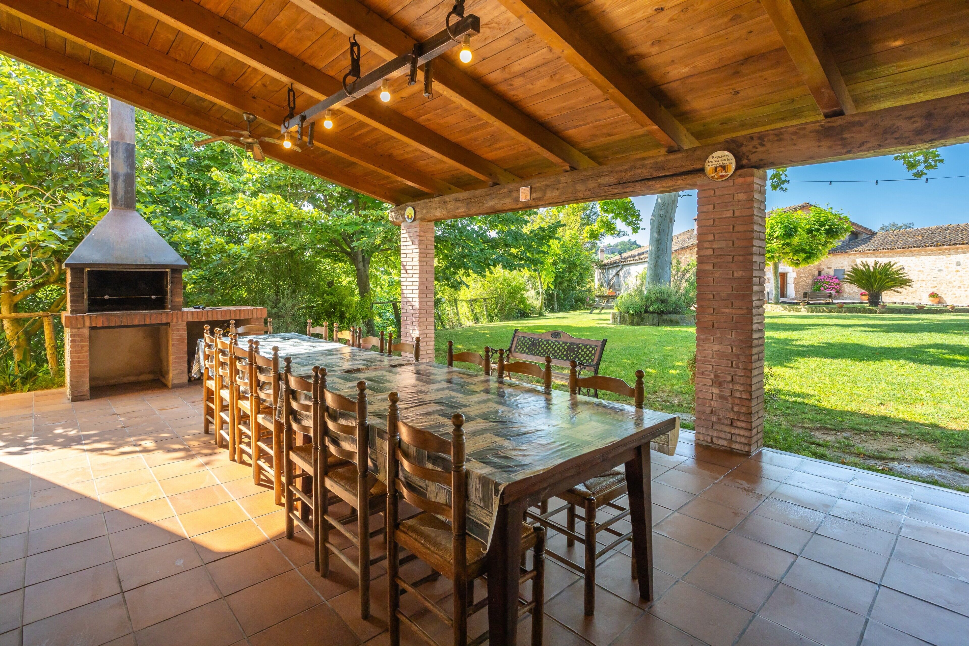 An outdoor patio with a brick oven, wooden table, and chairs.