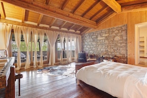 Ein Zimmer mit Holzboden, einem Bett, einem Klavier, einer Steinwand und einem Kamin.