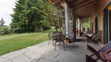 A covered patio with stone flooring, outdoor furniture, and a view of a green landscape.