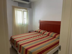 A single bed with a striped bedspread, a wooden headboard, a bedside table, and a window with curtains.