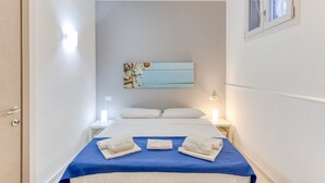Een hotelkamer met een bed, een nachtkastje, een wandairconditioner en een ingelijst schilderij.