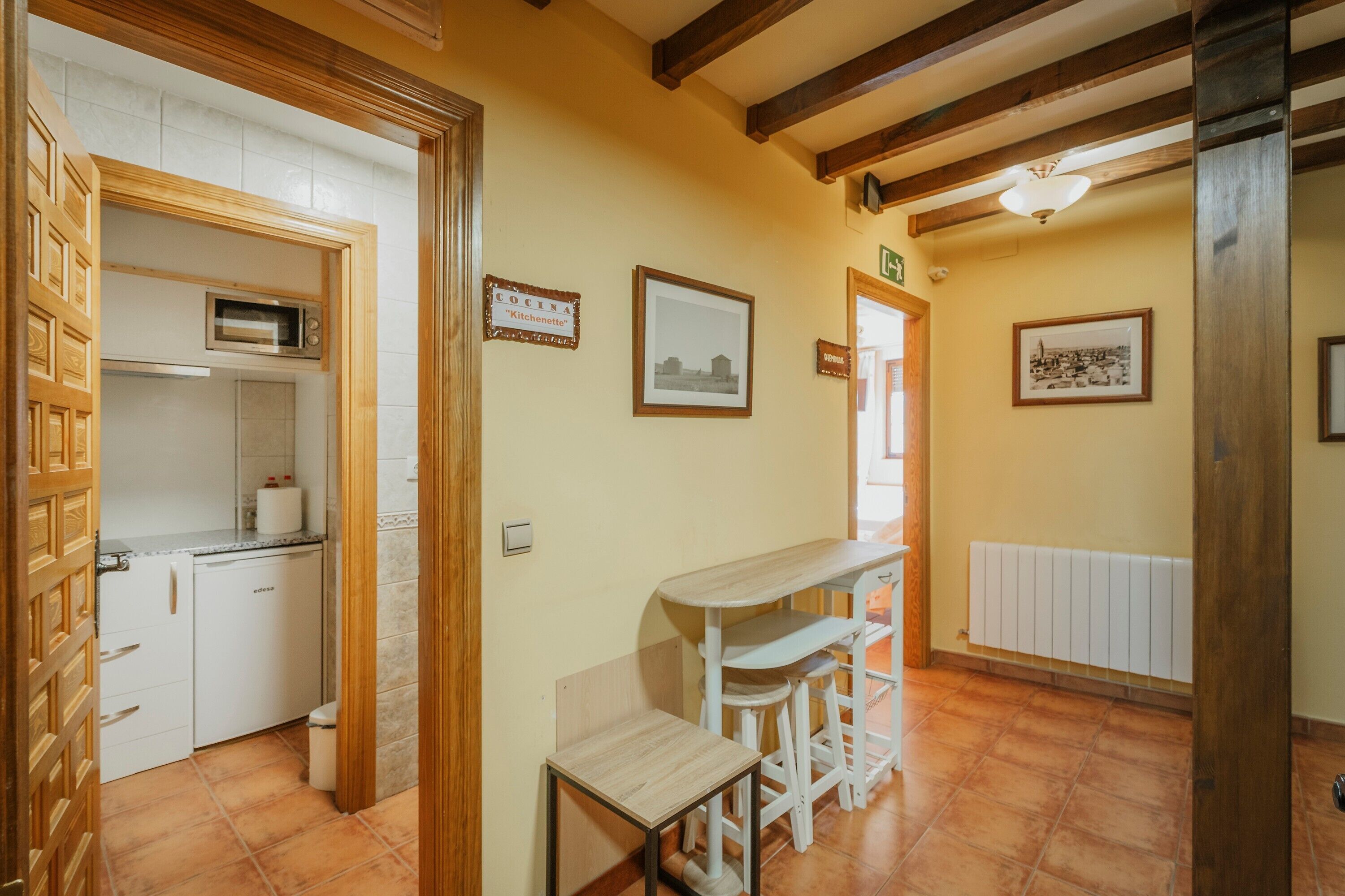 A kitchen with a microwave, a small table with stools, and framed pictures on the walls.