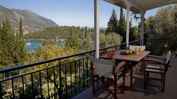 Een balkon met een tafel en stoelen, met uitzicht op een meer en bergen.