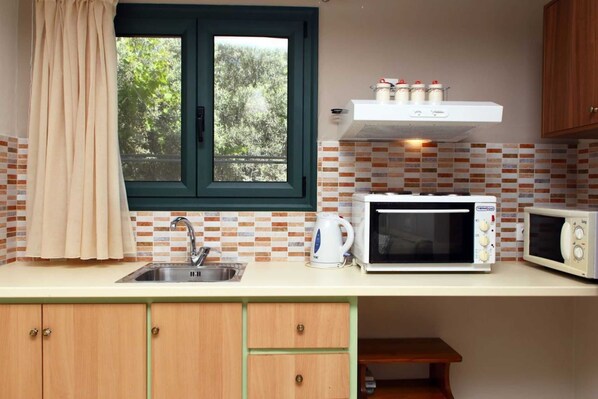 A compact kitchen with a window, a sink, a kettle, a microwave, and a cabinet.