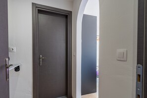 A hallway with a closed door, a light switch, and a power outlet on the wall. - Room 'Relaxroom 2' with Shared Garden, Wi-Fi and Air Conditioning (Lefkimmi)