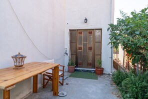 Pieni patio, jossa on puinen pöytä ja tuolit, ruukussa oleva kasvi sekä koristeellisella säleiköllä varustettu ovi.