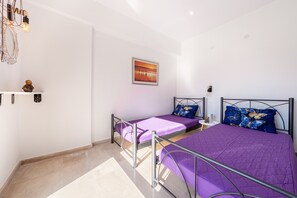 A bedroom with two beds, a wall-mounted shelf with a figurine, a framed picture, and a small table with a lamp. - Room 'Relaxroom 2' with Shared Garden, Wi-Fi and Air Conditioning (Lefkimmi)