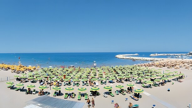 Ein Strand mit vielen grünen und gelben Sonnenschirmen, Liegestühlen und einem klaren, blauen Himmel.