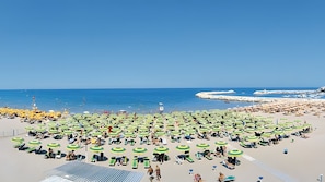 Une plage parsemée de nombreux parasols verts et jaunes, de chaises longues et sous un ciel bleu azur.