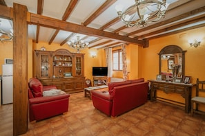 Una sala de estar con vigas de madera, un televisor, sofás rojos y un aparador con puertas de cristal.