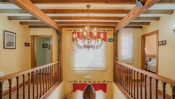 Un pasillo con vigas de madera, un candelabro, una cortina roja y un letrero que indica una habitación.