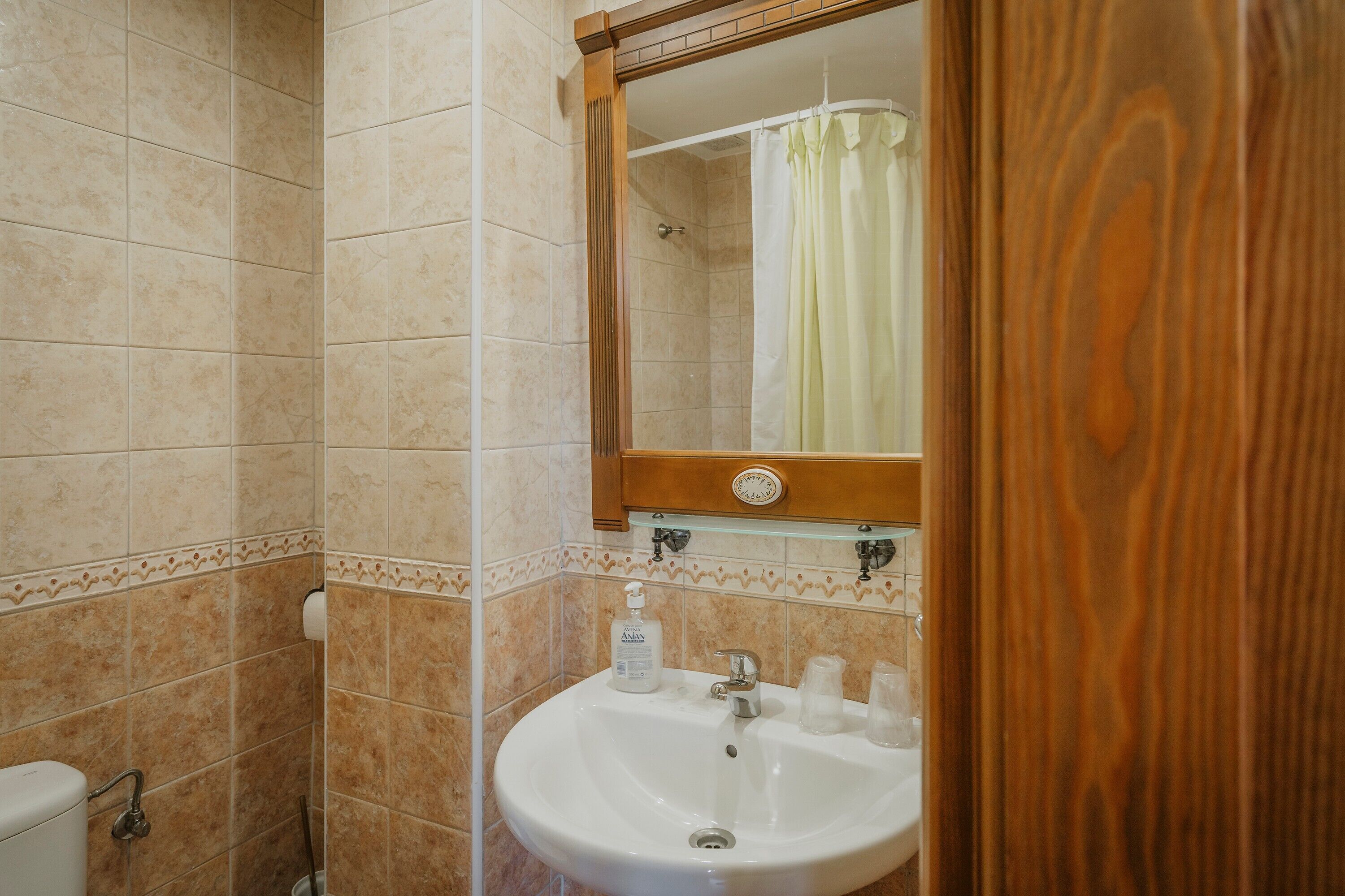 Een badkamer met een wastafel, spiegel, douchegordijn en betegelde wanden.