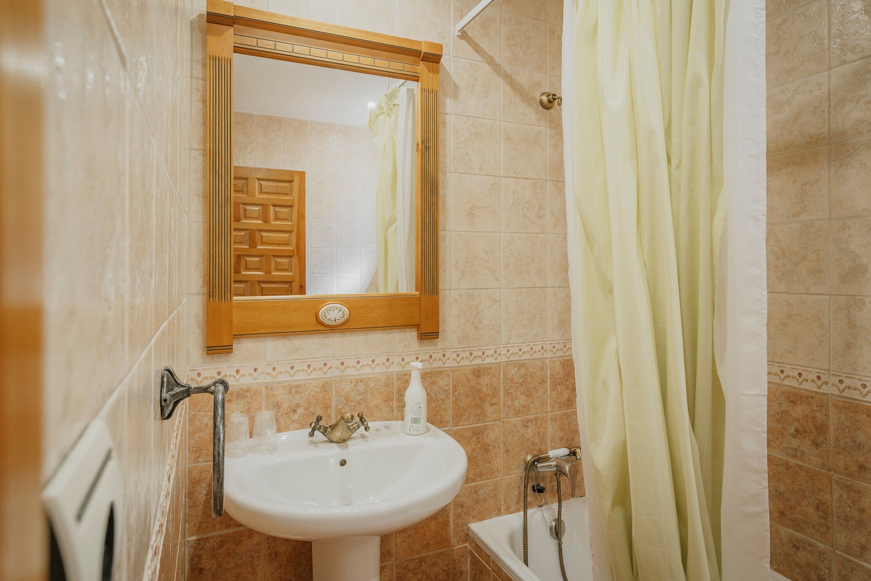 Een badkamer met een wastafel, spiegel, douchegordijn en handdoekhouder.