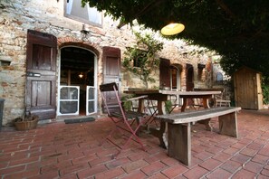 Een terras buiten met een stenen gebouw, houten banken en een tafel.
