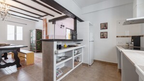Una cocina moderna con armarios blancos, horno empotrado y comedor con mesa y banco de madera.