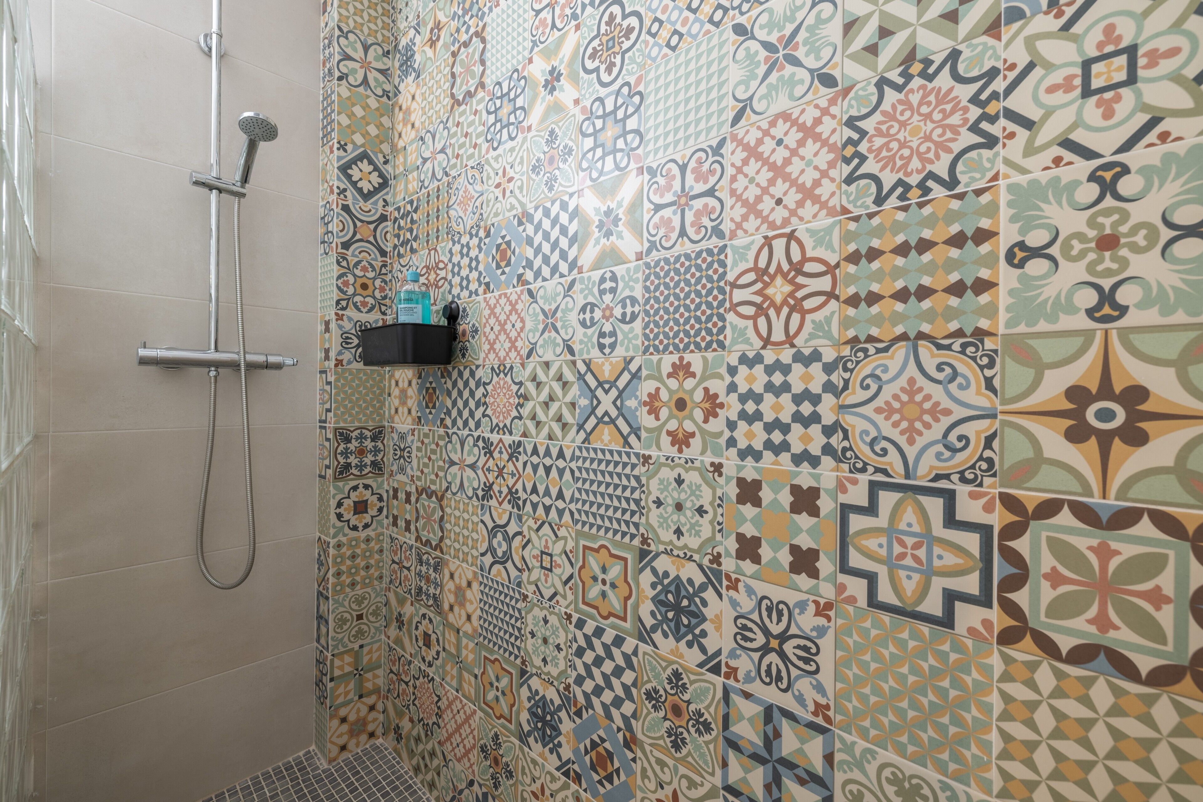 Une douche équipée d’un pommeau de douche à main et d’un mur recouvert de différents types de carreaux décoratifs.